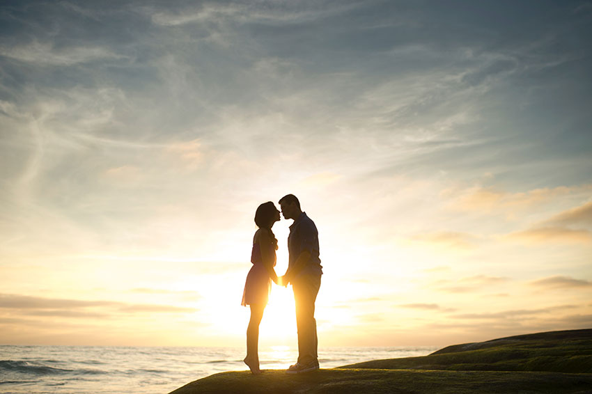 Man and woman standing by the sea holding hands at sunset