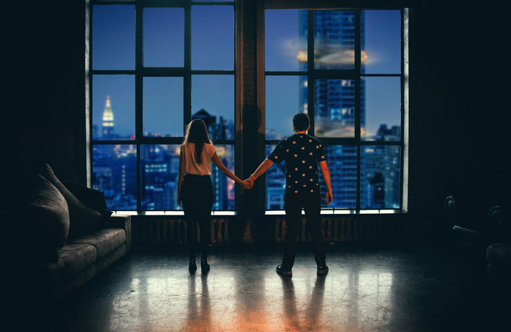 Couple standing far apart looking out at city holding hands