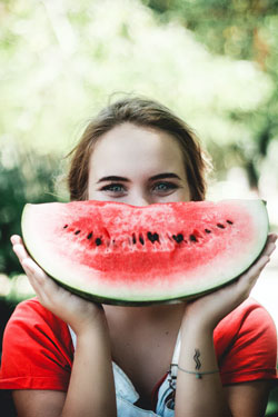 Woman holding a slice of watermelon in front of her mouth, creating the impression of a smile