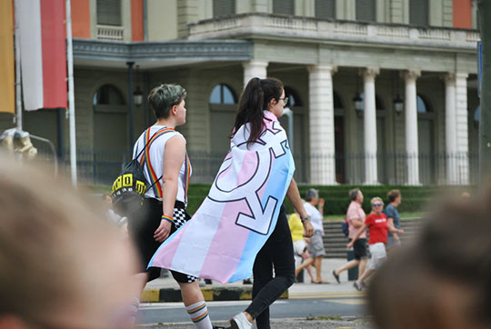 A person wearing the transgender flag as a cape.