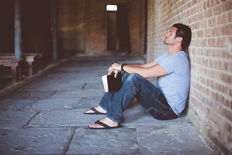 Man leaning against a wall while sitting holding a journal