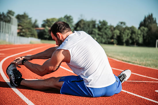 A man stretching his legs while sitting down on an outdoor track.