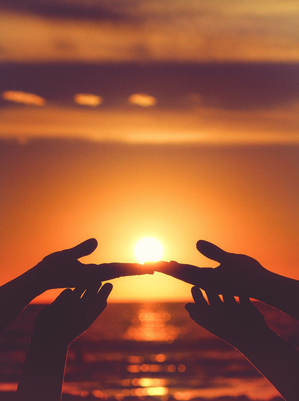 People holding hands up in front of an ocean sunset