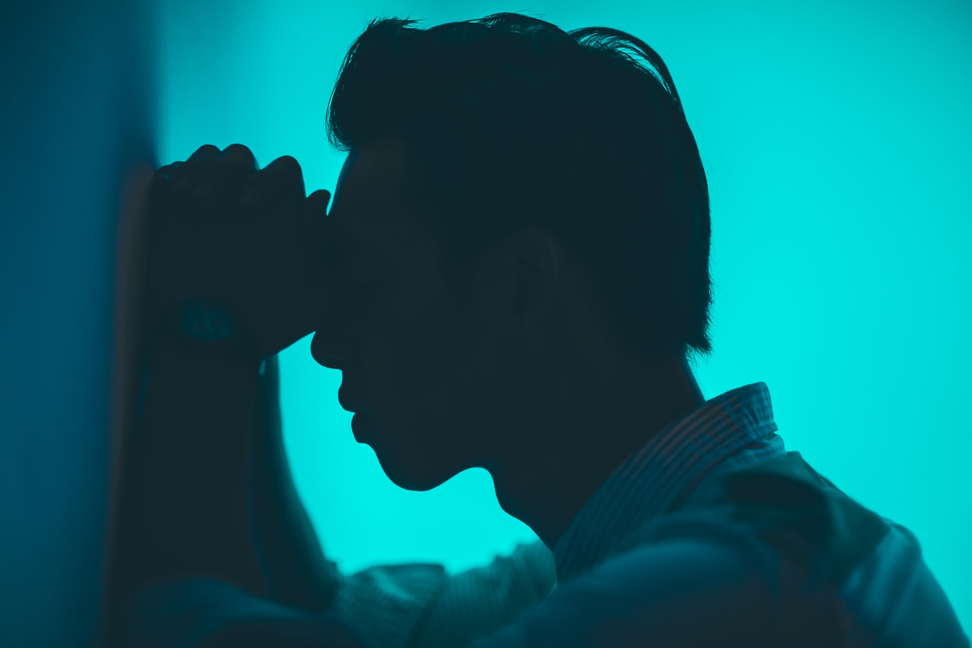 A stressed man leaning against a wall with forehead on his fists