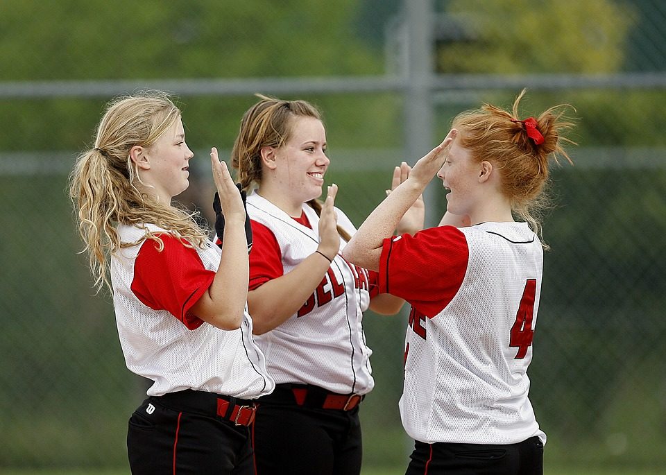 Three happy teenagers celebrating after a softball game.