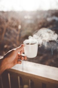 hand holding steaming cup of coffee on patio