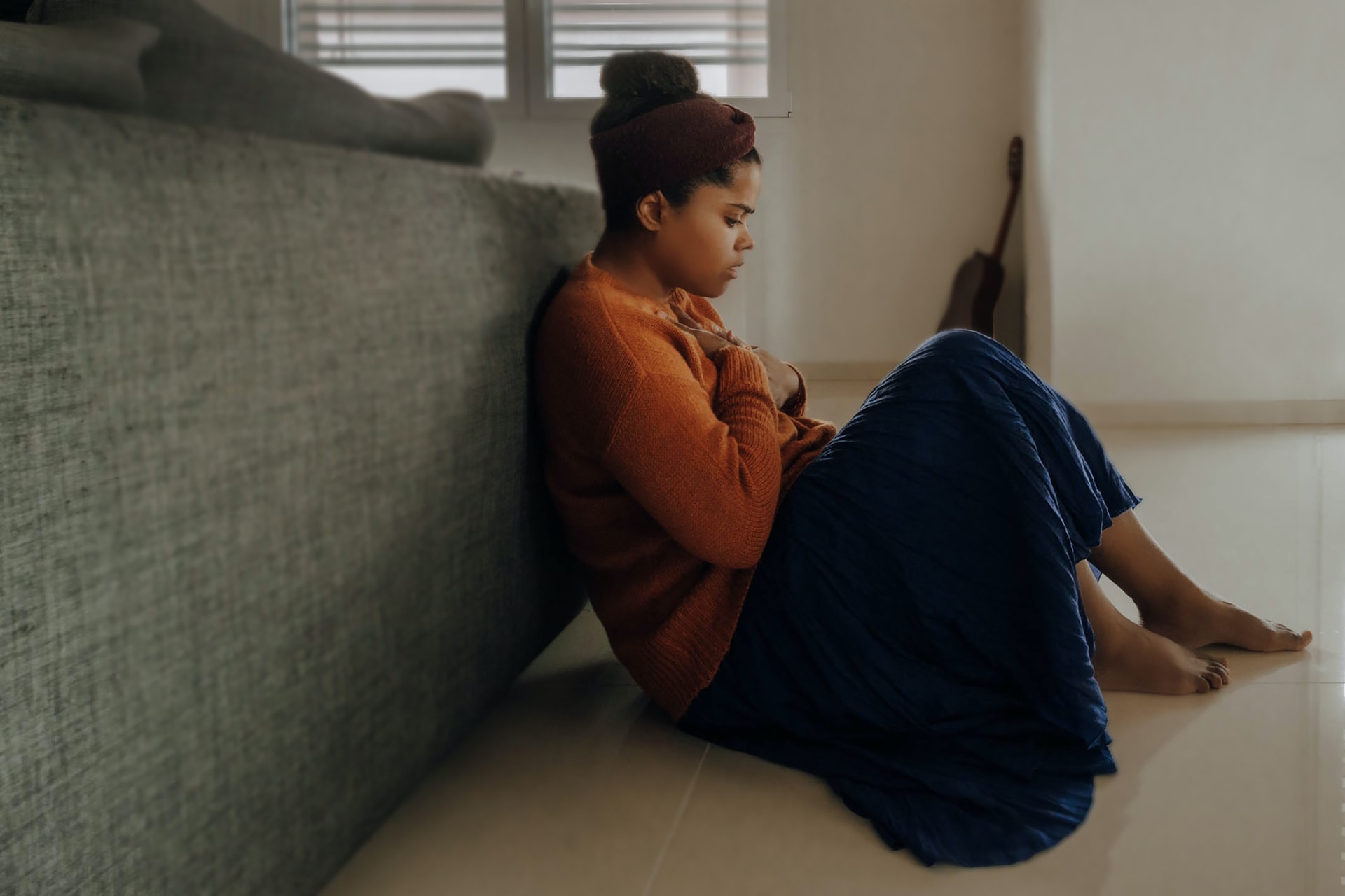 A woman in orange and blue sits on the floor forlornly