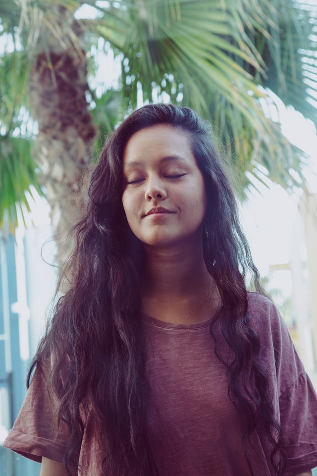 Young person closing their eyes with palm trees behind them