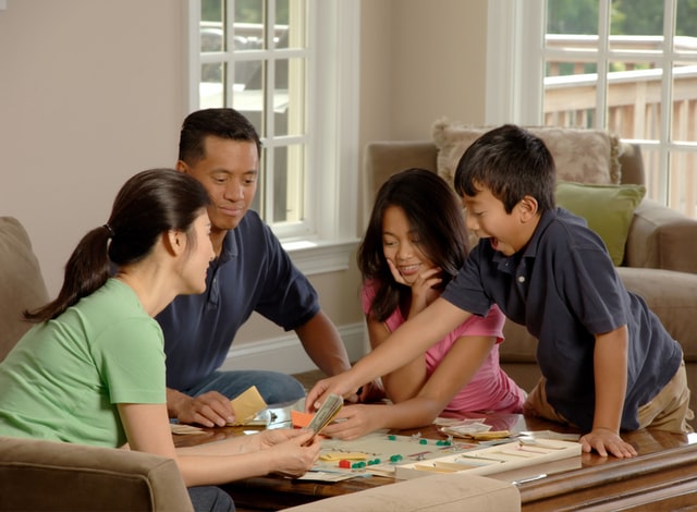 A family of one man, one woman, a boy, and a girl play a board game in a living room