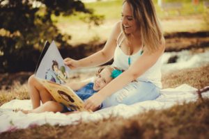Mother sitting outdoors, reading a book to her daughter