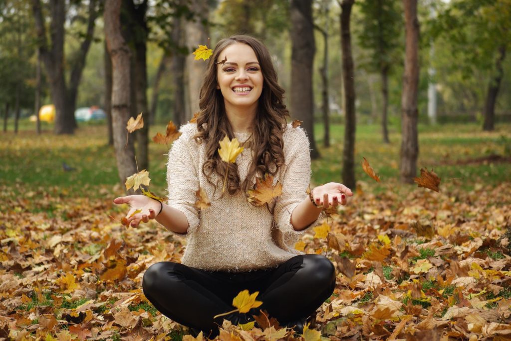 Smiling Woman Sitting On Ground With Leaves