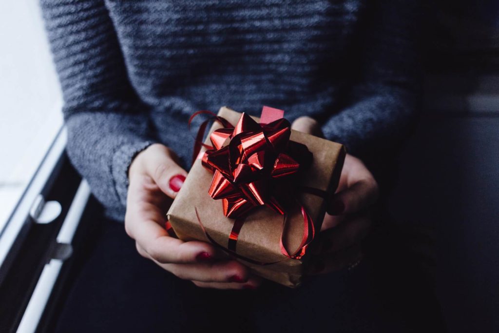Person in grey sweater holding a gift wrapped box with red ribbon