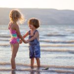Two children standing on the beach holding hands
