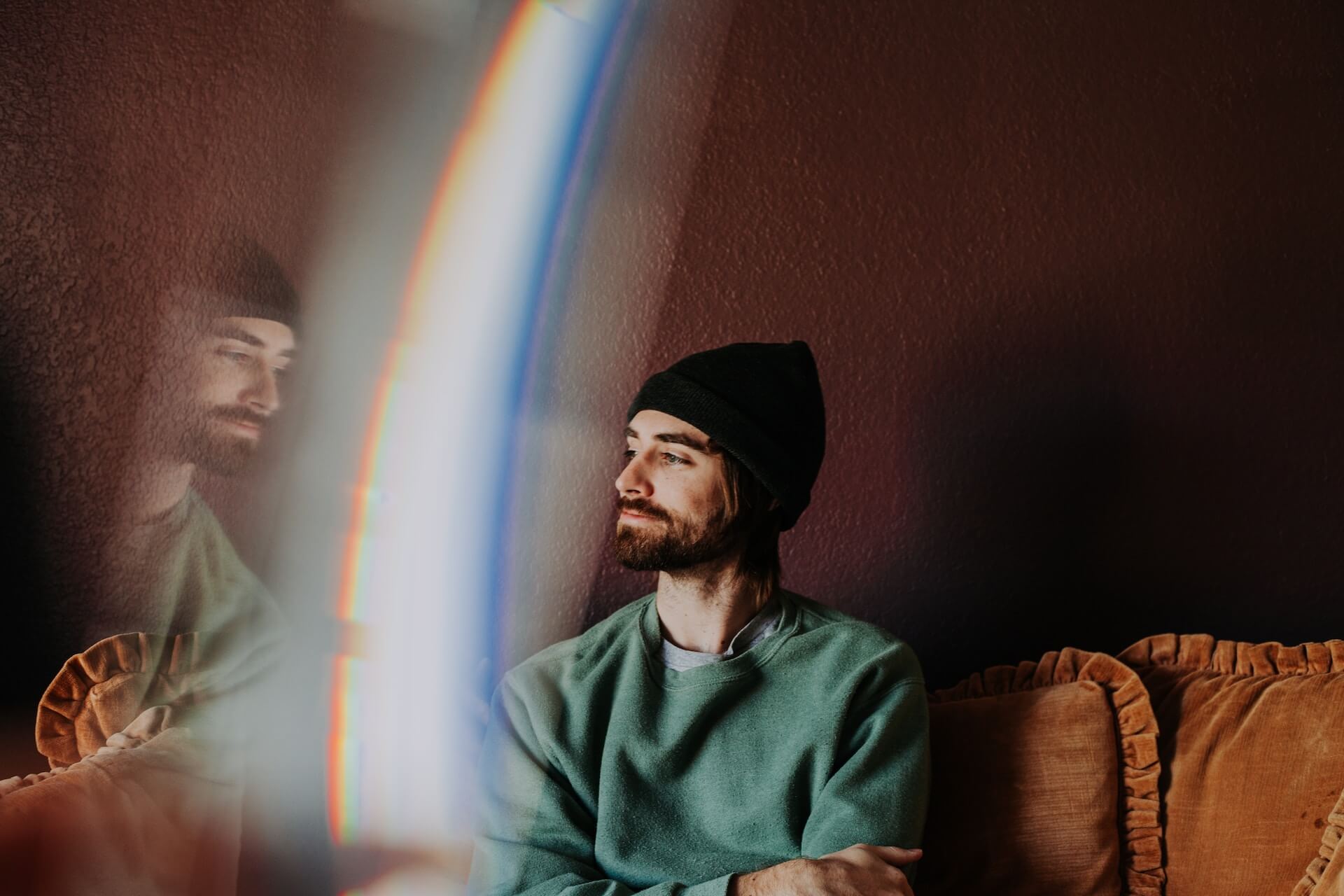 Person wearing a black beanie and green sweater looking thoughtful with lense flare reflection