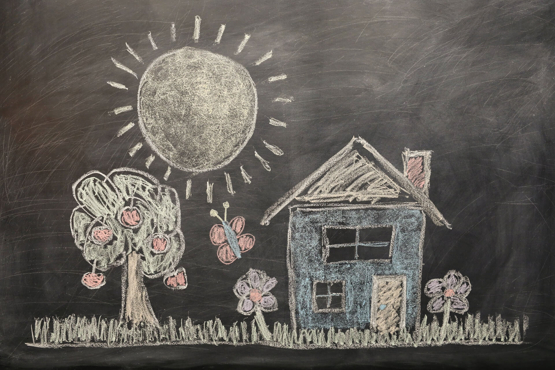 Chalk drawing on a blackboard of a person’s childhood home with trees and a sun