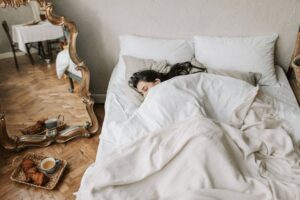 Woman sleeping under bed covers with a tray of food on the floor
