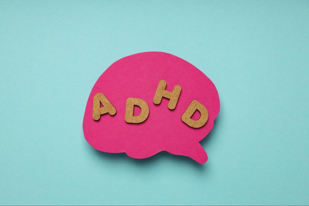 Cork letters that spell out “ADHD” on a pink paper brain cutout