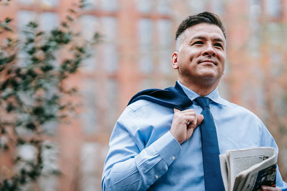 A man in a blue tie holds a newspaper outdoors