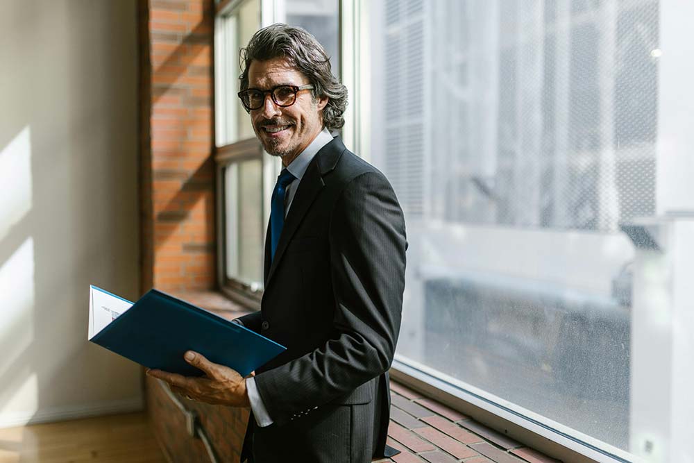 A man stands in front of a window holding a folder