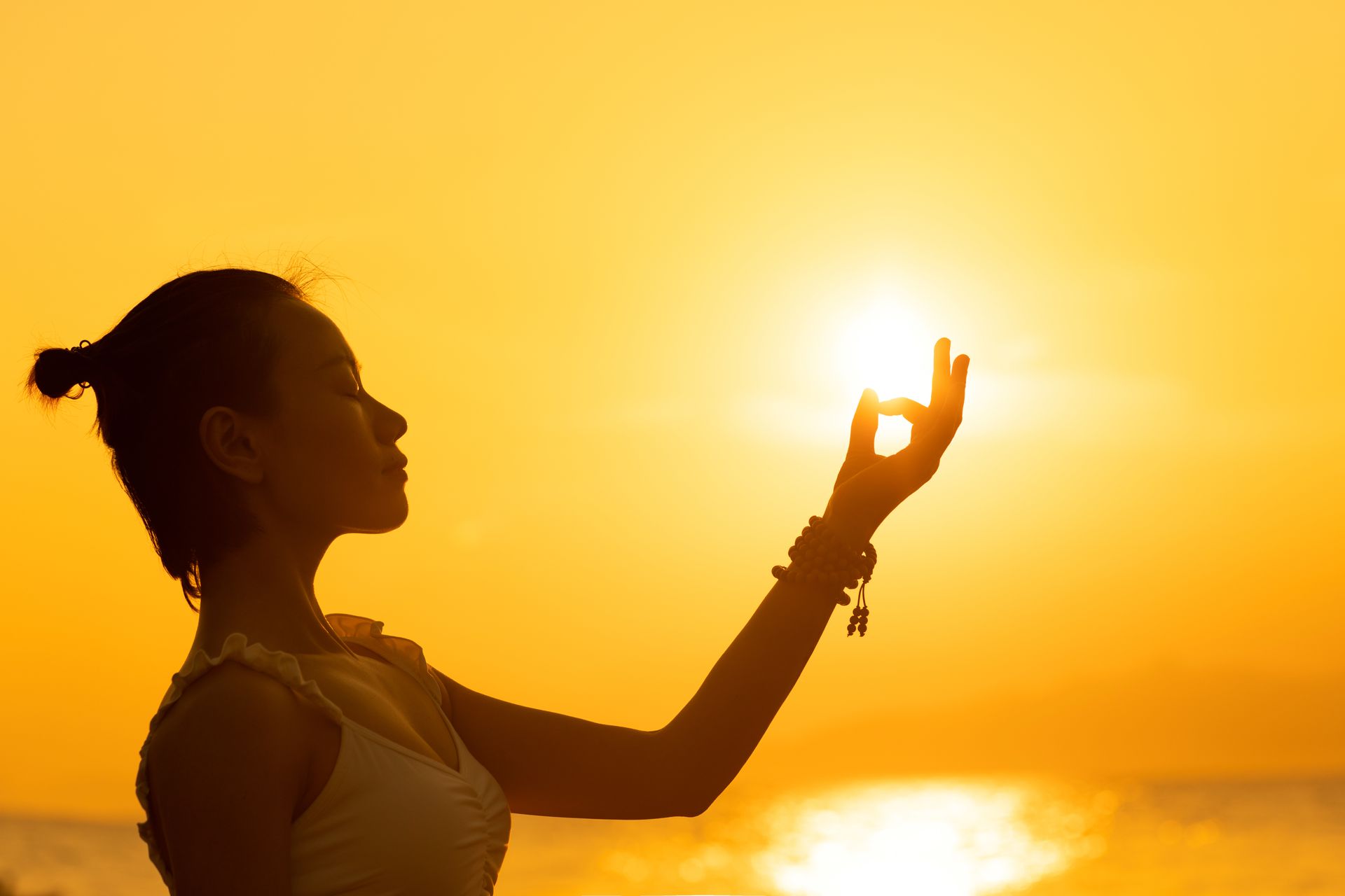 A woman meditates in front of a setting sun and bright orange sky